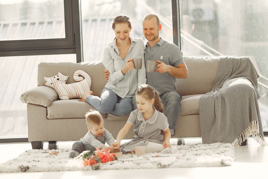 Cheerful family wearing casual clothes sitting in living room while playing and drinking tea during weekend at home in morning